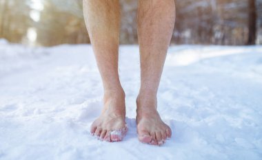 Cold training and acclimation concept. Senior guy standing barefoot on snow at winter forest, cropped view clipart
