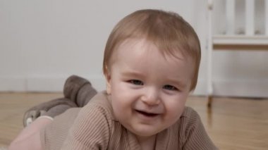 Sevimli bir bebek göbeğinde yere uzanmış, kameraya gülüyor, portreyi kapatıyor, ağır çekimde