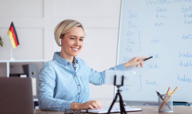 Çevrimiçi dil okulu. İnternette Almanca dersi veren, akıllı telefon kullanan, öğrencilere dil bilgisini açıklayan kadın öğretmen.