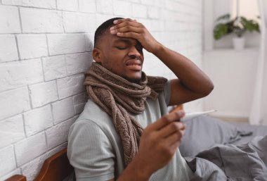 Adamın elinde termometre var. Evde yatakta ateşi var.