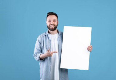 Reklam panosu reklamı. Gülümseyen genç adamın portresi boş beyaz posteri gösteriyor. Tasarımınız için yer var.