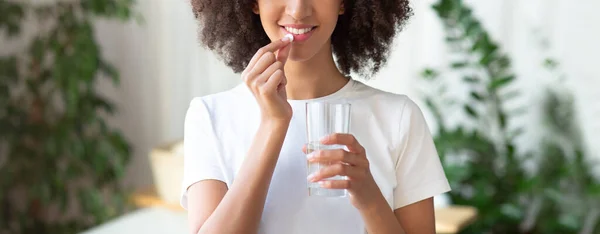 Joyeux jeune femme afro-américaine prend une pilule de vitamines et de boissons avec un verre d'eau — Photo