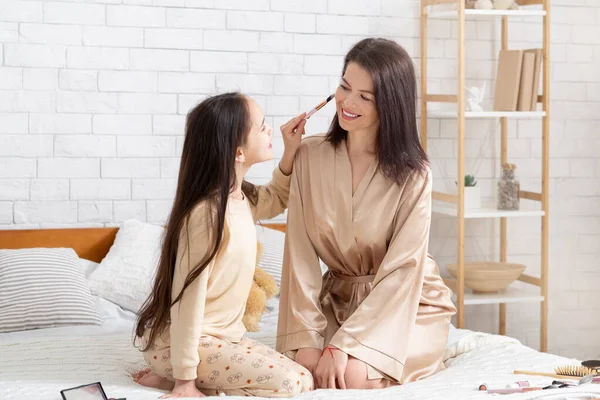 Tiempo de vinculación familiar. Linda chica adolescente aplicando polvo en la mejilla de sus mamás, usando maquillaje en el día de la belleza en casa —  Fotos de Stock