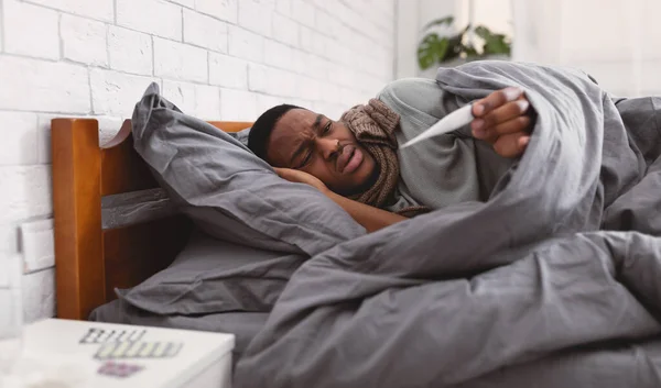 Zieke zwarte man meten temperatuur hebben koorts in bed binnen — Stockfoto