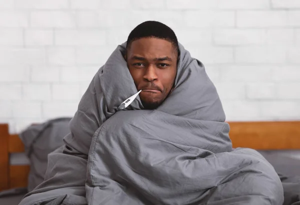 Malo chico africano sosteniendo termómetro en la boca sentado en el dormitorio — Foto de Stock