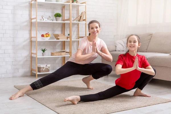 Home quarantine workout. Positive mom and her happy teen daughter stretching their legs in living room, blank space