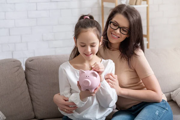 Feliz madre y su linda hija adolescente poniendo moneda en la hucha, ahorrando dinero en casa, espacio para copiar —  Fotos de Stock