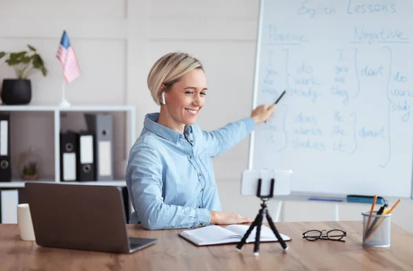 Professora feliz dando aula de inglês on-line de casa, apontando para quadro-negro, explicando regras gramaticais — Fotografia de Stock