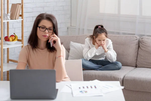 Занятая мать, работающая онлайн из дома, брошенная дочь-подросток, сидящая рядом на диване, страдающая от одиночества — стоковое фото