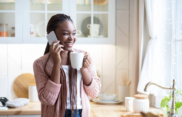 Manhã relaxante. preto mulher falando no celular e beber café no cozinha — Fotografia de Stock