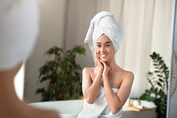 Szczęśliwy millenium Afroamerykanka kobieta z ręcznikiem na głowie, z czystej świeżej skóry dotyka twarzy — Zdjęcie stockowe