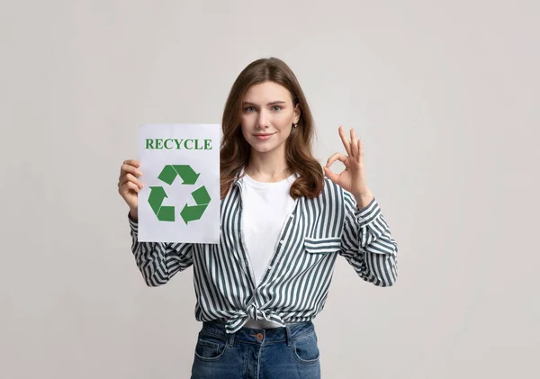Lächelnde Dame hält Motivationsplakat mit Recycle-Zeichen und zeigt Ok-Geste — Stockfoto