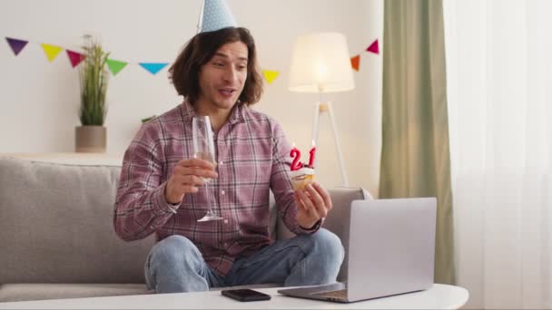 Happy guy in party hat video calling to friends, holding cupcake with 21 number and drinking champagne, online születésnap — Stock videók