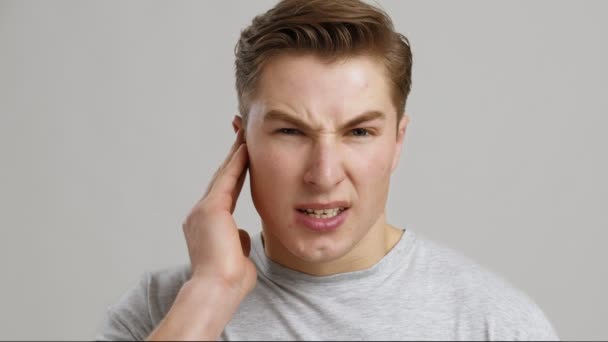 Otitis. Kulak ağrısından muzdarip genç bir adamın portresi, yakın plan, gri arka plan — Stok video