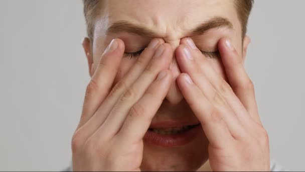Reakcja alergiczna. Zbliżenie portret młodego mężczyzny pocierającego bolące oczy, zwolnione tempo, szare tło — Wideo stockowe