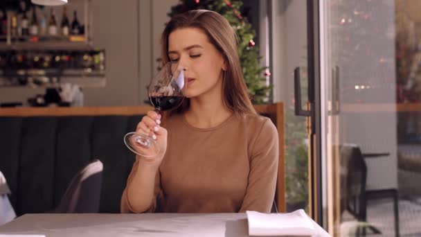 若い美しい女性は、赤ワインのガラスを楽しんで、カフェに座って、カメラに笑みを浮かべて — ストック動画
