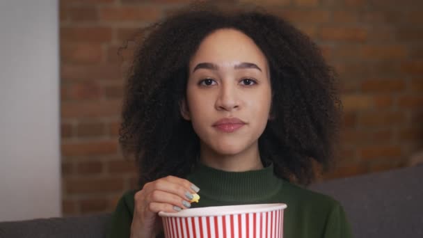 Primer plano retrato de una joven afroamericana viendo películas y comiendo palomitas de maíz, cámara lenta — Vídeos de Stock