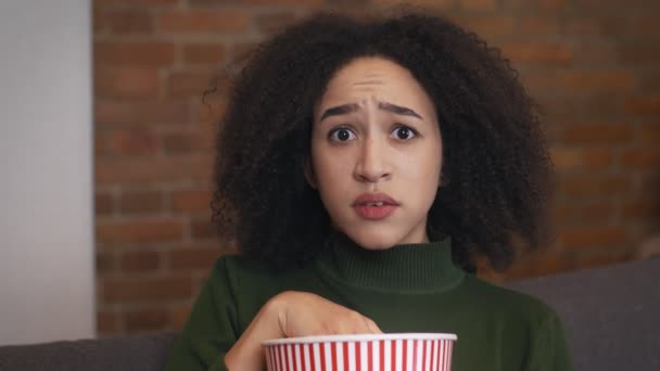 Νεαρή συναισθηματική μαύρη γυναίκα που βλέπει τηλεόραση στο σπίτι και τρώει ποπ κορν, νιώθει φοβισμένη και φοβισμένη, κλείνει το πορτραίτο — Αρχείο Βίντεο
