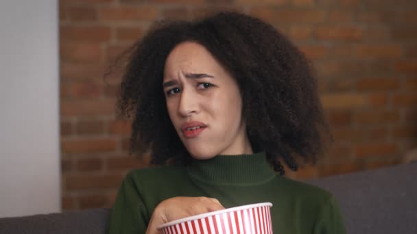 Close up portrait of displease black woman watching show at home and eating popcorn, expressing negativity, slow motion — Stock Video