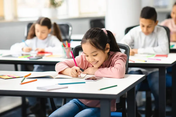 Portrait of small asian girl sitting at desk in classroom — Stock Photo, Image