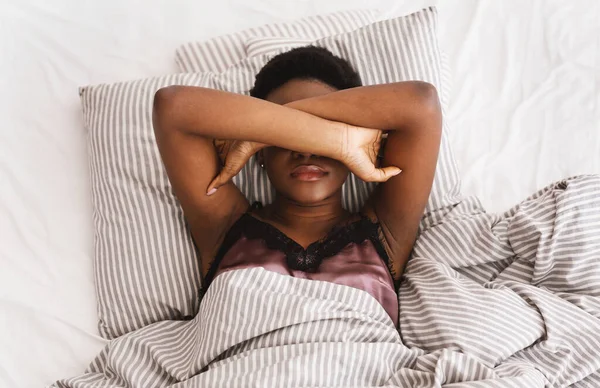 Sleepless young woman suffering from insomnia, lying on bed, covering eyes with hands, trying to sleep — Stock Photo, Image
