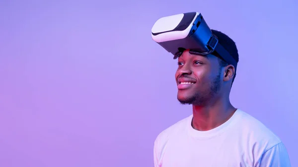 Sorrindo afro-americano cara vestindo óculos VR e olhando para o lado, luz de néon — Fotografia de Stock