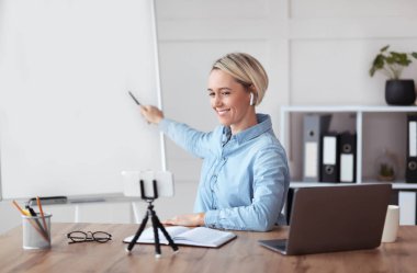 Neşeli genç öğretmen evden online özel ders veriyor. Tasarımınız için boş tahtaya işaret ediyor.