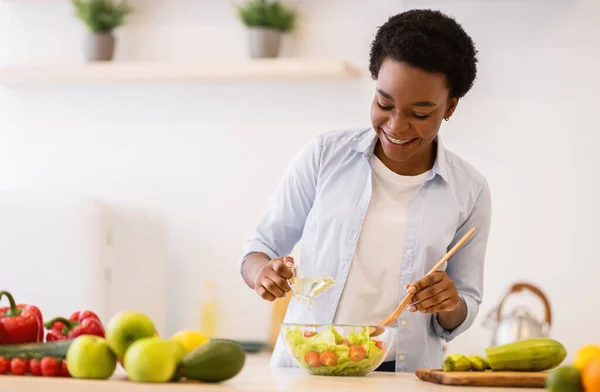 Счастливая черная женщина готовит здоровый овощной салат, стоящий на кухне — стоковое фото