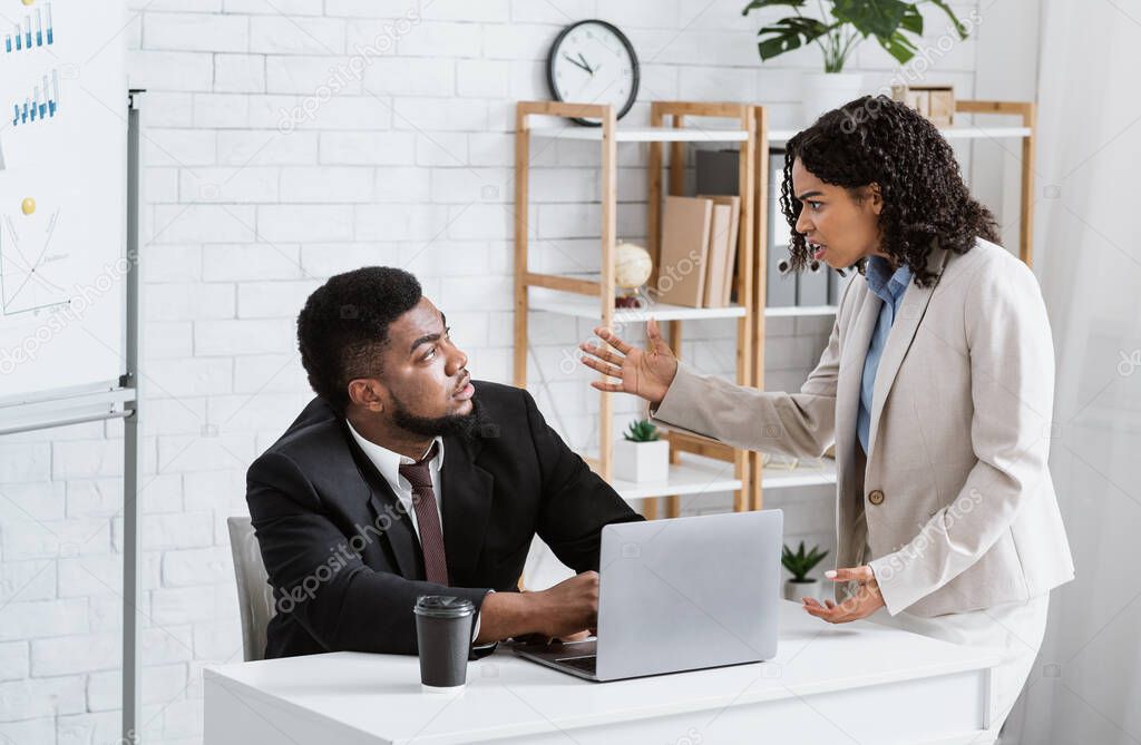 Angry African American lady boss scolding male employee for error in urgent project at office. Workplace stress concept