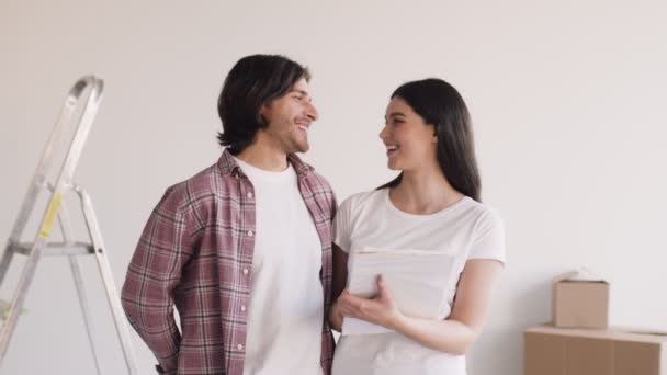 Gelukkig getrouwd stel dat elkaar aankijkt en lacht om de camera, knuffelt in een nieuw eigen appartement, houdt documenten vast — Stockvideo