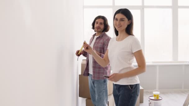 Casado homem e mulher medindo parede com fita adesiva juntos, fazendo a melhoria da casa e renovação — Vídeo de Stock
