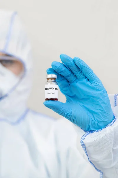 Medic in hazmat pak, handschoenen, masker en bril houdt vaccin tegen covid-19 — Stockfoto