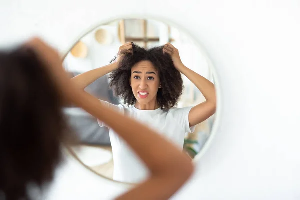 Upset young cute excited female touches curly hair and disappointed, look in reflection of round mirror — Stock Photo, Image