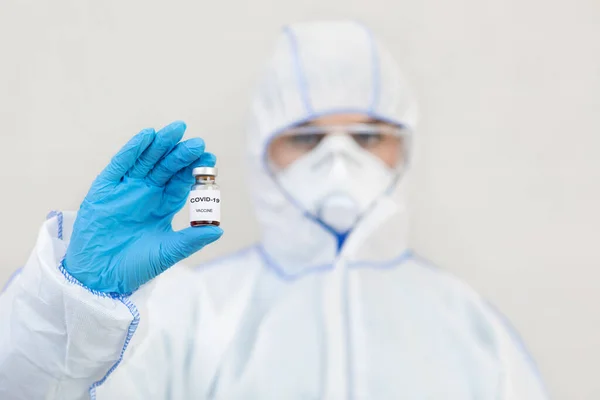 Médico en traje de materiales peligrosos, guantes, máscara protectora y gafas sostiene vacuna contra Covid-19 — Foto de Stock