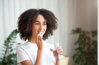 Mutlu gülümseyen Afro-Amerikan kadını Omega-3 ile morina yağı ya da vitamin alıyor.