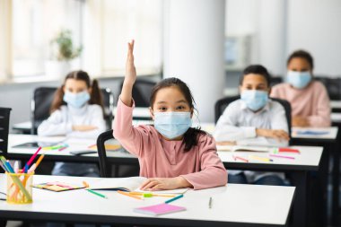 Sınıfta el kaldıran çocuklar, tıbbi maske takıyorlar.