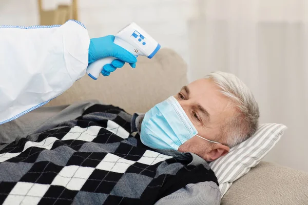 Doctor en traje de materiales peligrosos mide la temperatura con un termómetro moderno sin contacto — Foto de Stock