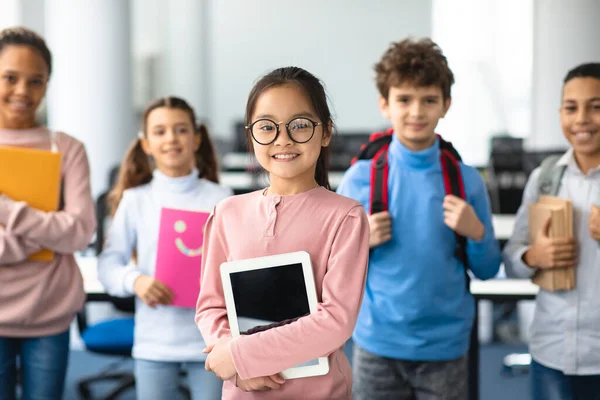 Uśmiechnięta azjatycka dziewczyna trzyma tablet stojąc z kolegami z klasy — Zdjęcie stockowe