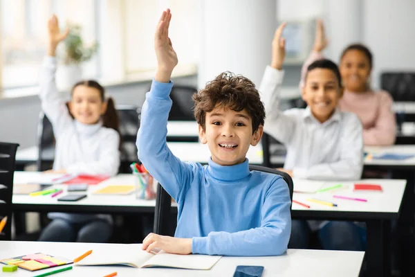 Diversi piccoli scolari alzare le mani in classe — Foto Stock
