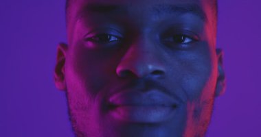 Neon ışıkta kameraya bakıp gülümseyen Afrikalı Amerikalı adamın portresini yakından çek.