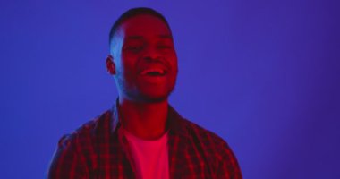 Pozitif Afrikalı Amerikalı adam neon ışıklarda dans ediyor, kameraya gülümsüyor, hayattan zevk alıyor, neon ışıkları var.