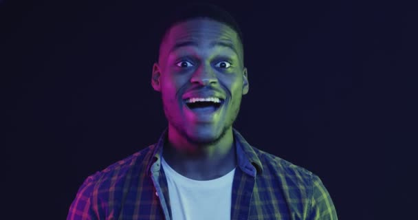 Närbild porträtt av emotionell afrikansk amerikansk kille röra kinderna i förvåning, neon ljus — Stockvideo