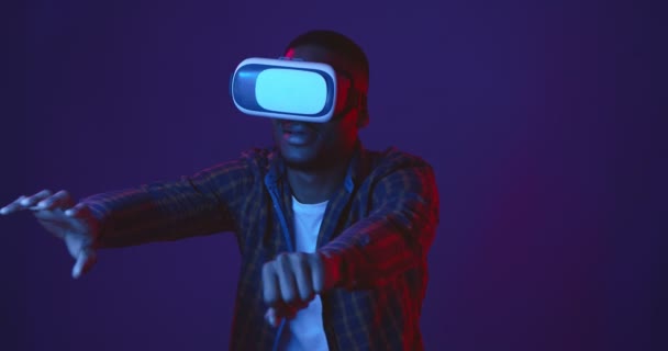 Studio shot of black guy wearing VR headset grabbing air with his hands, jouer au jeu vidéo pour attraper des signes, néons lumières — Video