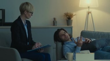 Bunalımlı bir adam, kişisel görüşmeler sırasında sorunları hakkında konuşuyor, kanepeye uzanıyor, psikolog notlar yazıyor.