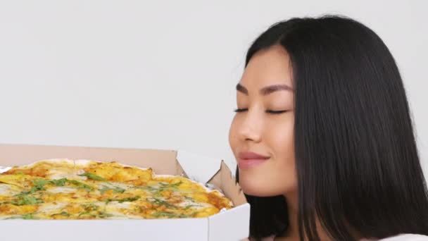 Mujer asiática oliendo la caja de espera de pizza cerca de la cara, fondo blanco — Vídeos de Stock