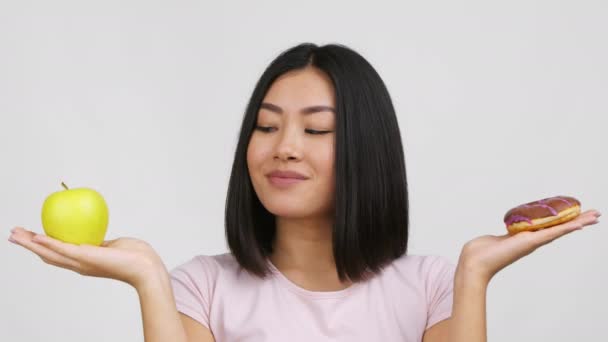 Mujer asiática elegir entre manzana y donut sobre fondo blanco — Vídeos de Stock