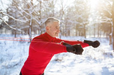 Kış parkında süspansiyon kayışlarıyla antrenman yapan atletik olgun adam.