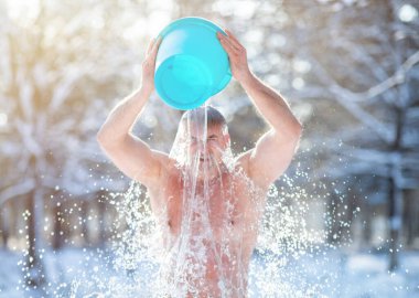 Senior man pouring water from bucket onto his head, tempering his body at snowy winter park clipart