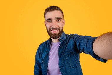 Yakışıklı beyaz adam selfie çekiyor ve turuncu stüdyo arka planında gülümsüyor.