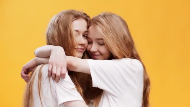Любовь к сестрам. Два одинаковых близнеца обнимаются на фоне оранжевой студии, наслаждаясь общением и единством — стоковое видео